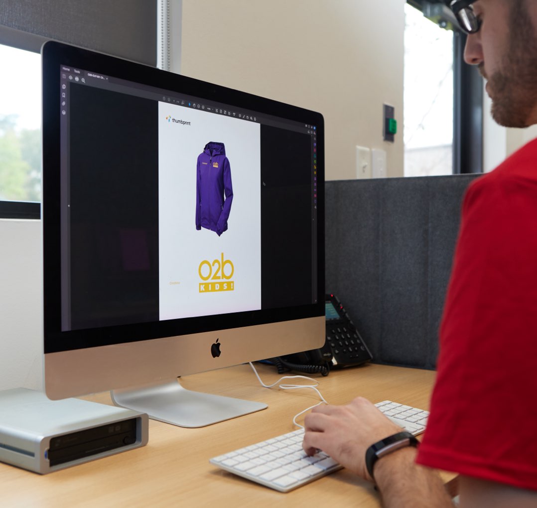 Person in red shirt designing a purple O2B Kids jacket on the computer