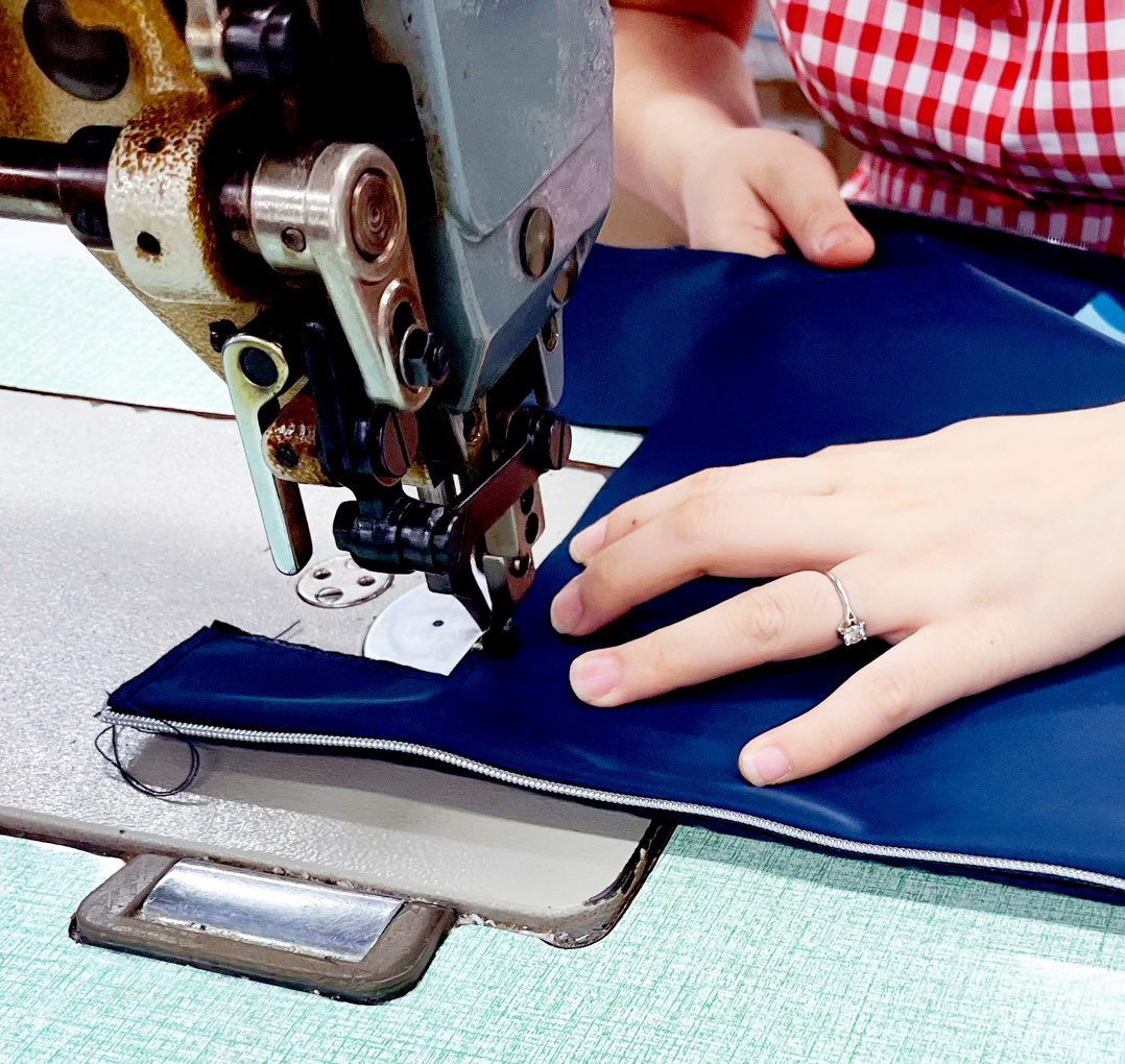 Close-up photo of a person using a sewing machine, sewing blue fabric.